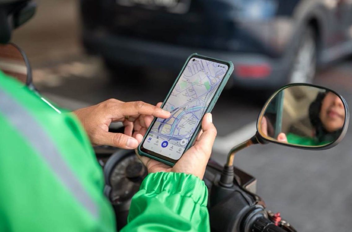 A rider’s hands holding a phone with the map app, the scooter mirror beside it