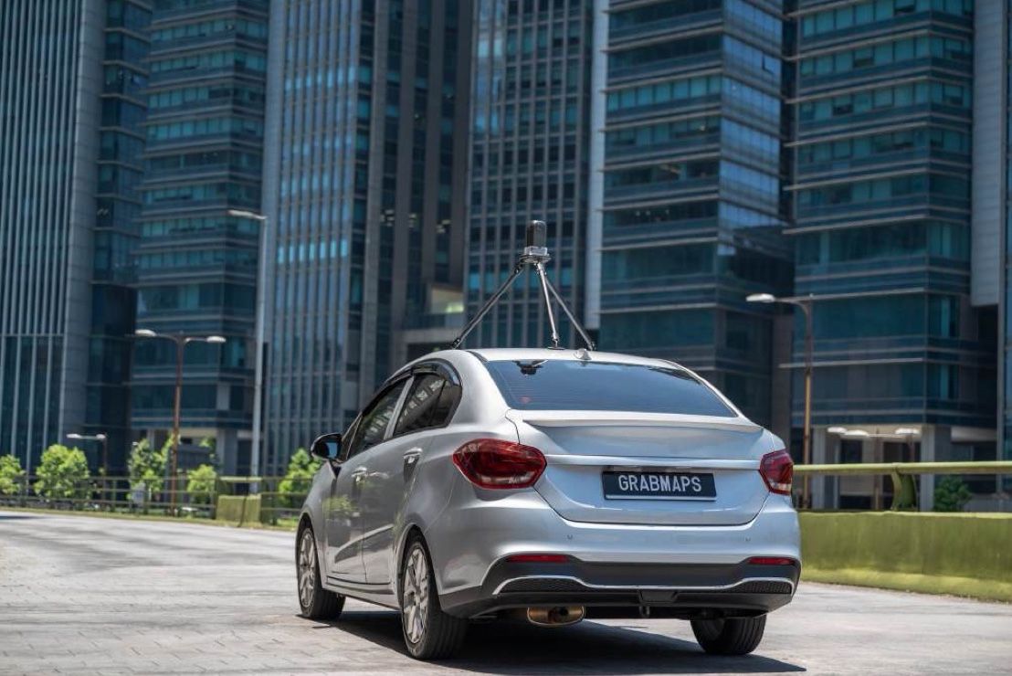 A silver GrabMaps car with a roof camera among office towers