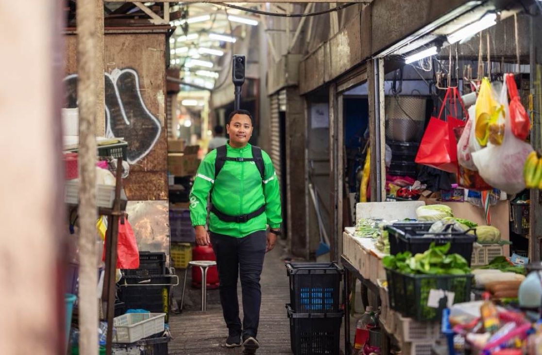 A mapper walks down a narrow wet-market alley with KartaCam on his backpack