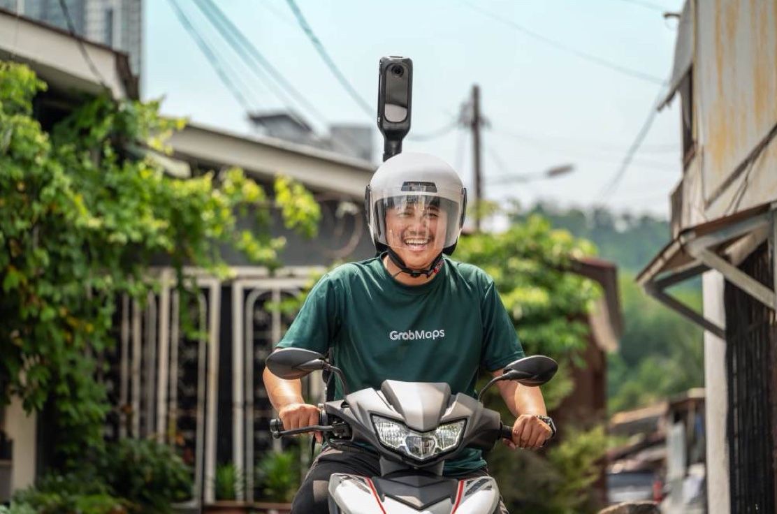 A laughing rider in a GrabMaps T-shirt on a scooter