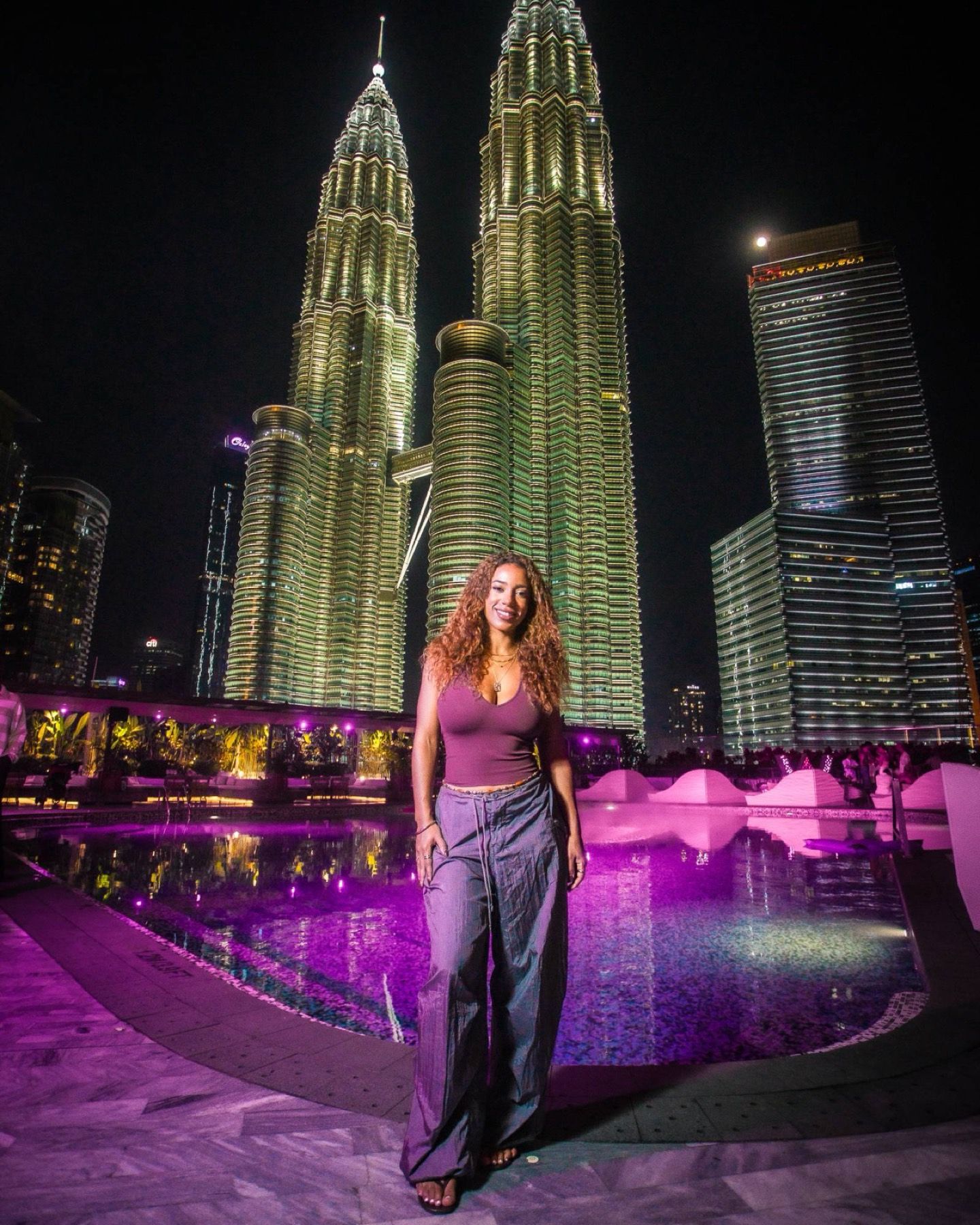 A guest by the pool at night with the Petronas Towers lit up behind her