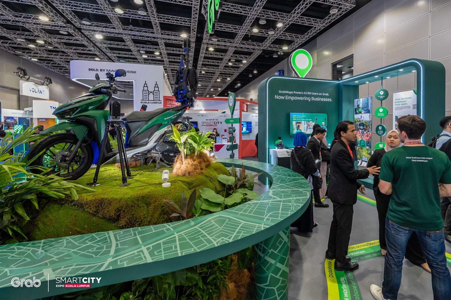 The centrepiece: a green Grab bike with KartaCam on a mossy rock, ringed by a map-printed counter