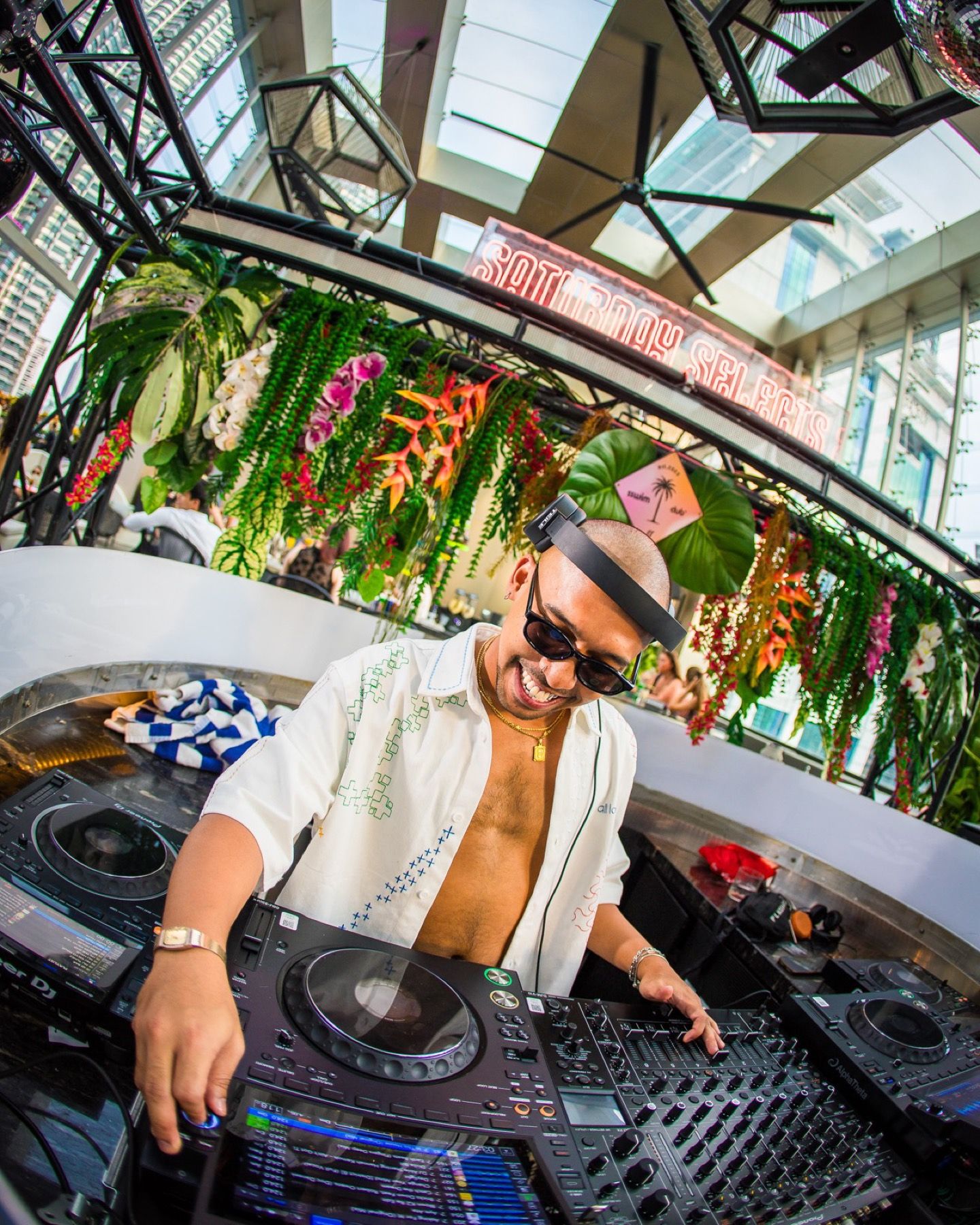 A DJ playing beneath flowers and giant leaves